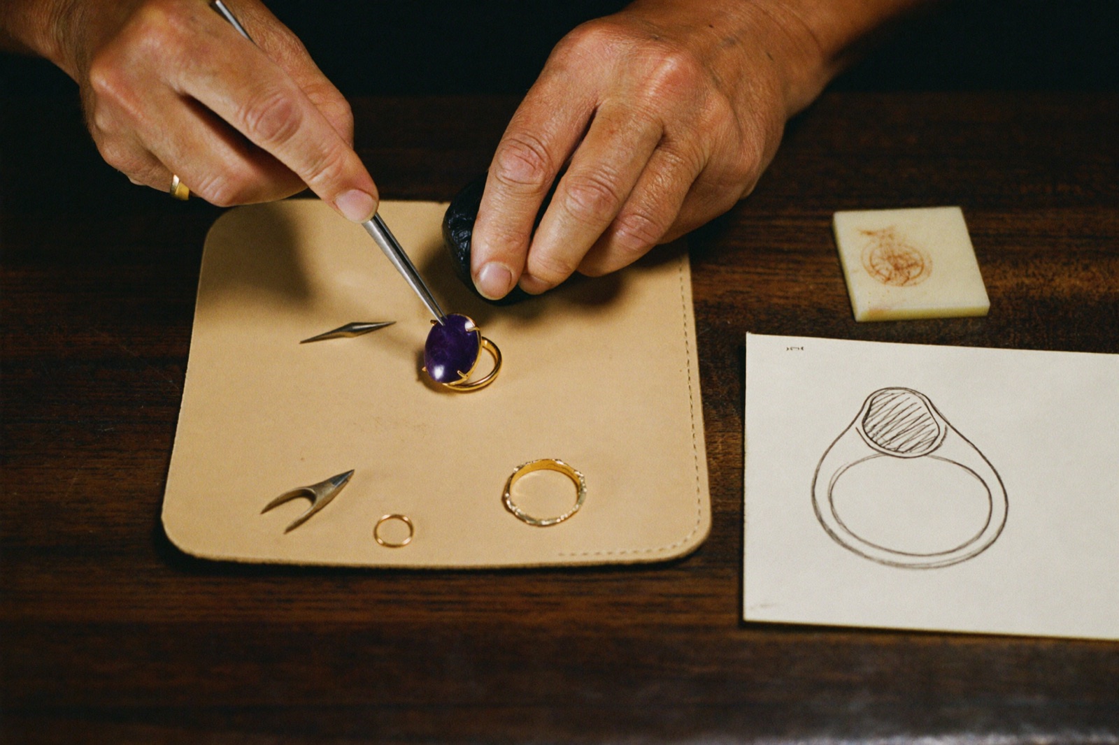 Master goldsmith's hands setting an amethyst into an 18kt gold ring on a leather pad